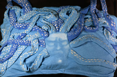 The lower back of a cotton jersey tank top in two shades of blue, sculpted with wild, curling snakes which wind around to the front and become shoulder straps