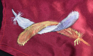 a white feather and a gold feather entwined, painted on maroon satin